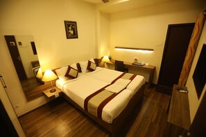 Une chambre d’hôtel avec un grand lit, des tables de chevet avec des lampes, un bureau avec une chaise et une porte.