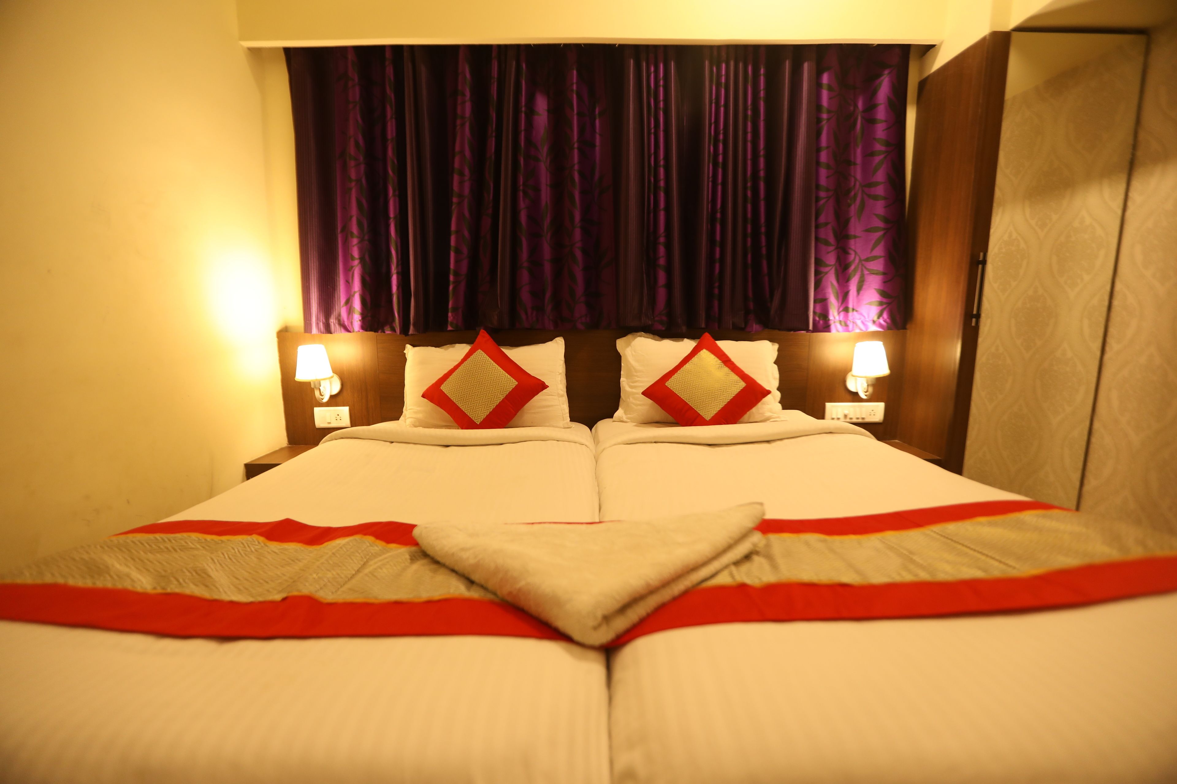 A double bed with a red and white bedspread, two pillows with red and white patterns, and two bedside lamps.