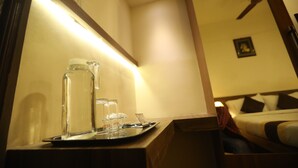 Ein Hotelzimmer mit einem Nachttisch, auf dem ein Tablett mit Gläsern und einer Wasserflasche steht. Im Hintergrund ist ein Deckenventilator zu sehen.