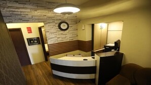 Ein Hotelzimmer mit Wand im Steinoptik, einem runden Bett, Holzboden, einer Uhr und einem Spiegel.