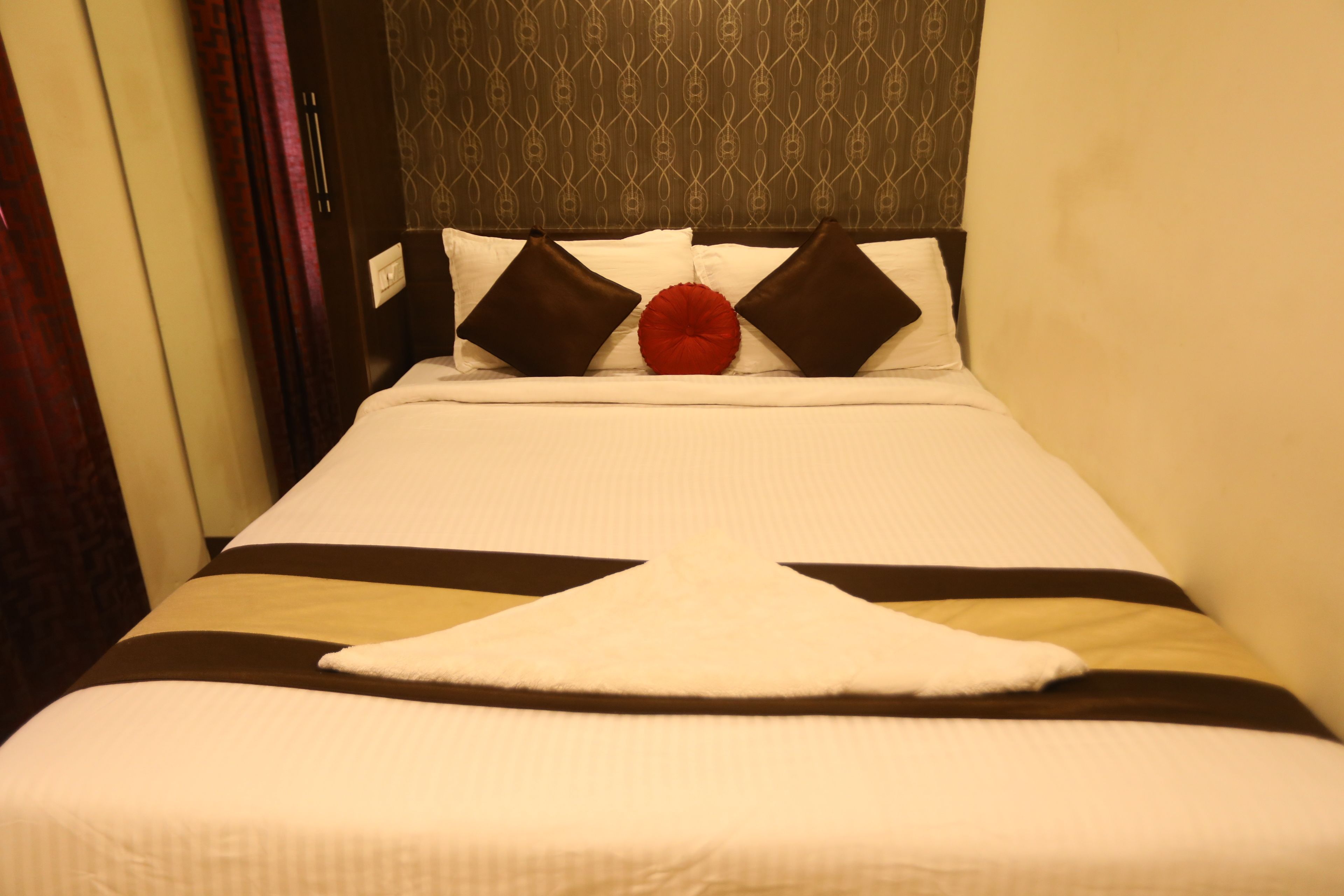 Habitación de hotel con una cama, cabecera de diseño estampado y almohada roja decorativa.