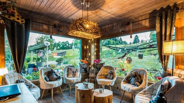 A cozy room with wooden floors, a large window, and a rustic chandelier. - Hotel Les 4 Saisons (Kruth)