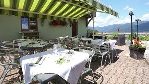 An outdoor dining area with tables and chairs, a striped awning, and a view of mountains. - Hotel Les 4 Saisons (Kruth)