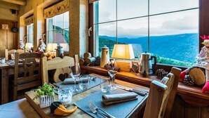 A dining area with a table set for two, a view of the mountains, and a rustic interior with wooden beams and a large window. - Hotel Les 4 Saisons (Kruth)