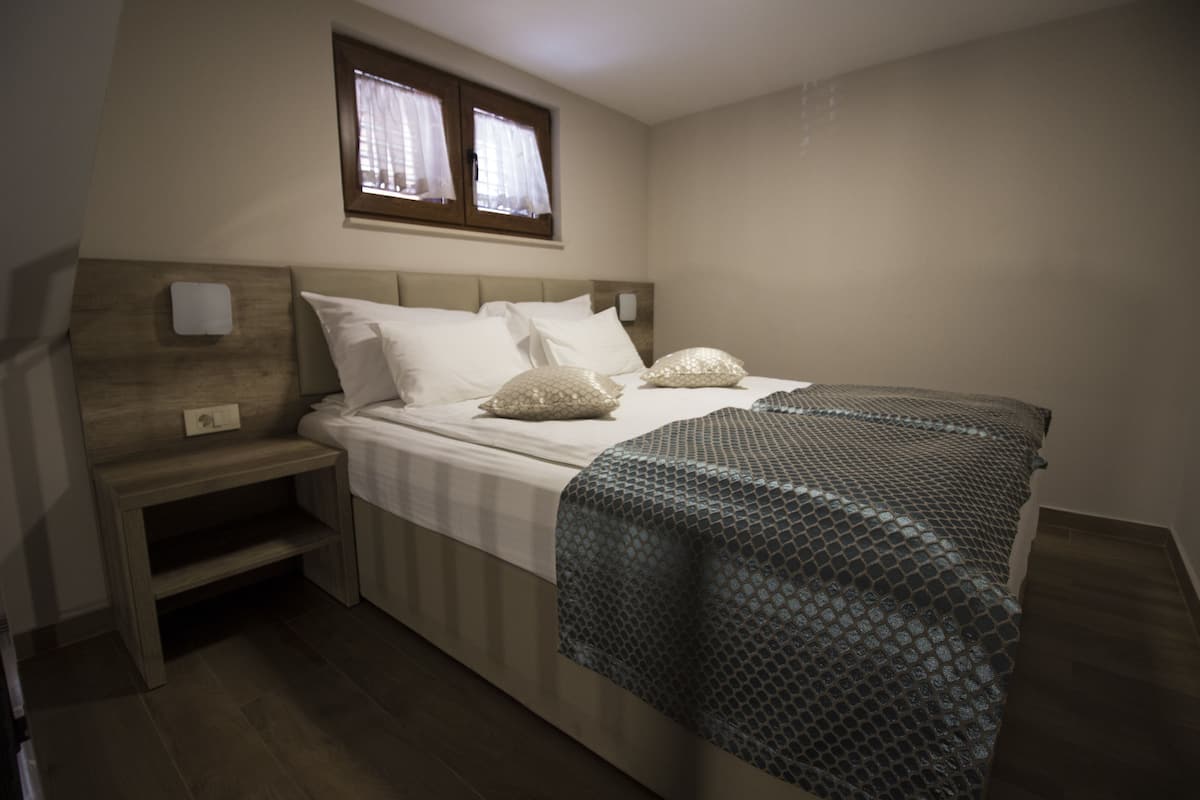 A bedroom with a bed, a nightstand, a window, and a wall-mounted light.