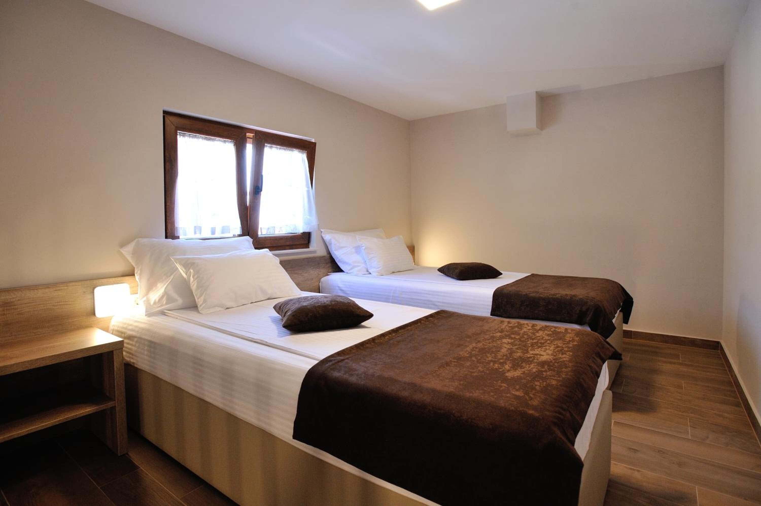 A room with two beds, a nightstand, and a window with curtains.