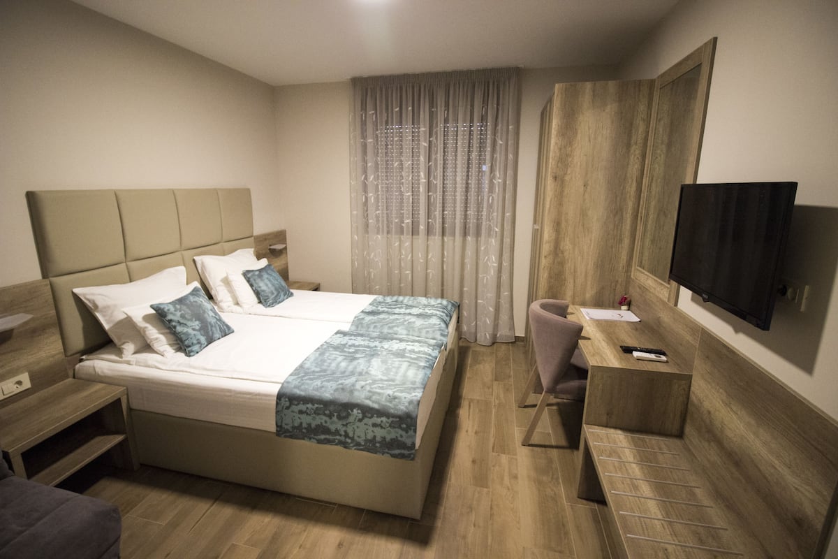 A hotel room with a bed, bedside table, chair, desk, TV, and curtains.