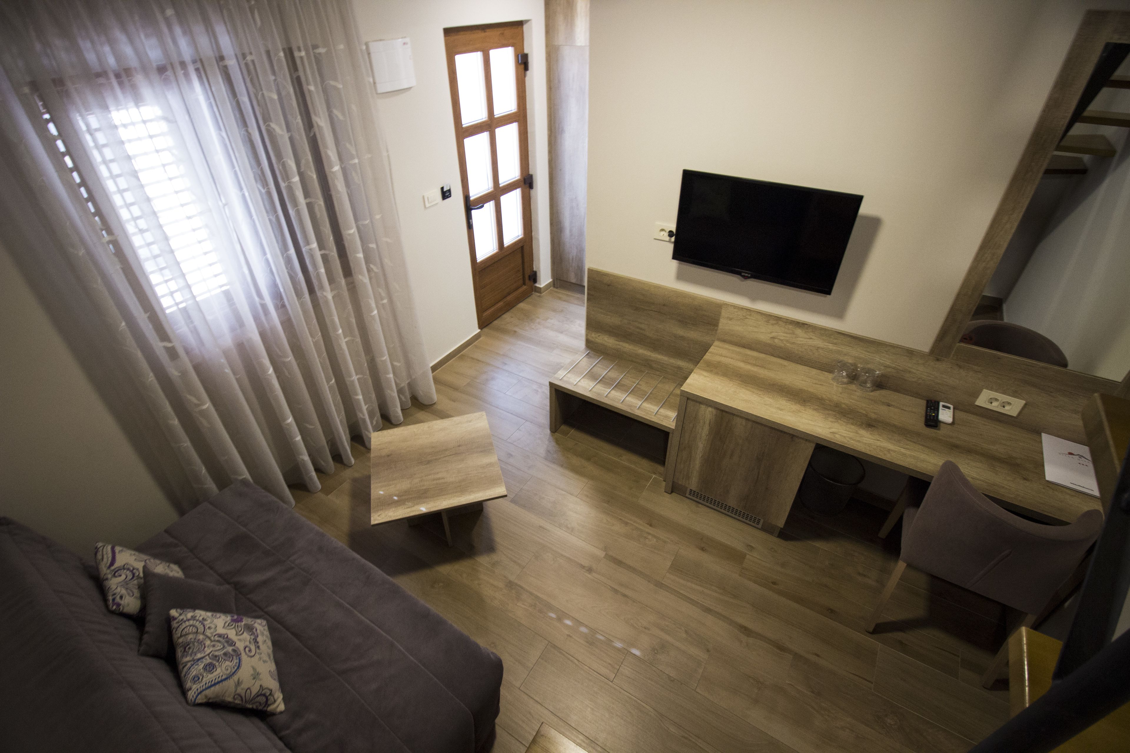 A modern living room with a sofa, a wooden dining table, and a TV mounted on the wall.