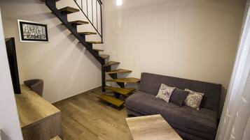 Un salon moderne avec un escalier en bois, un canapé gris agrémenté de coussins à motifs et une petite table basse en bois.