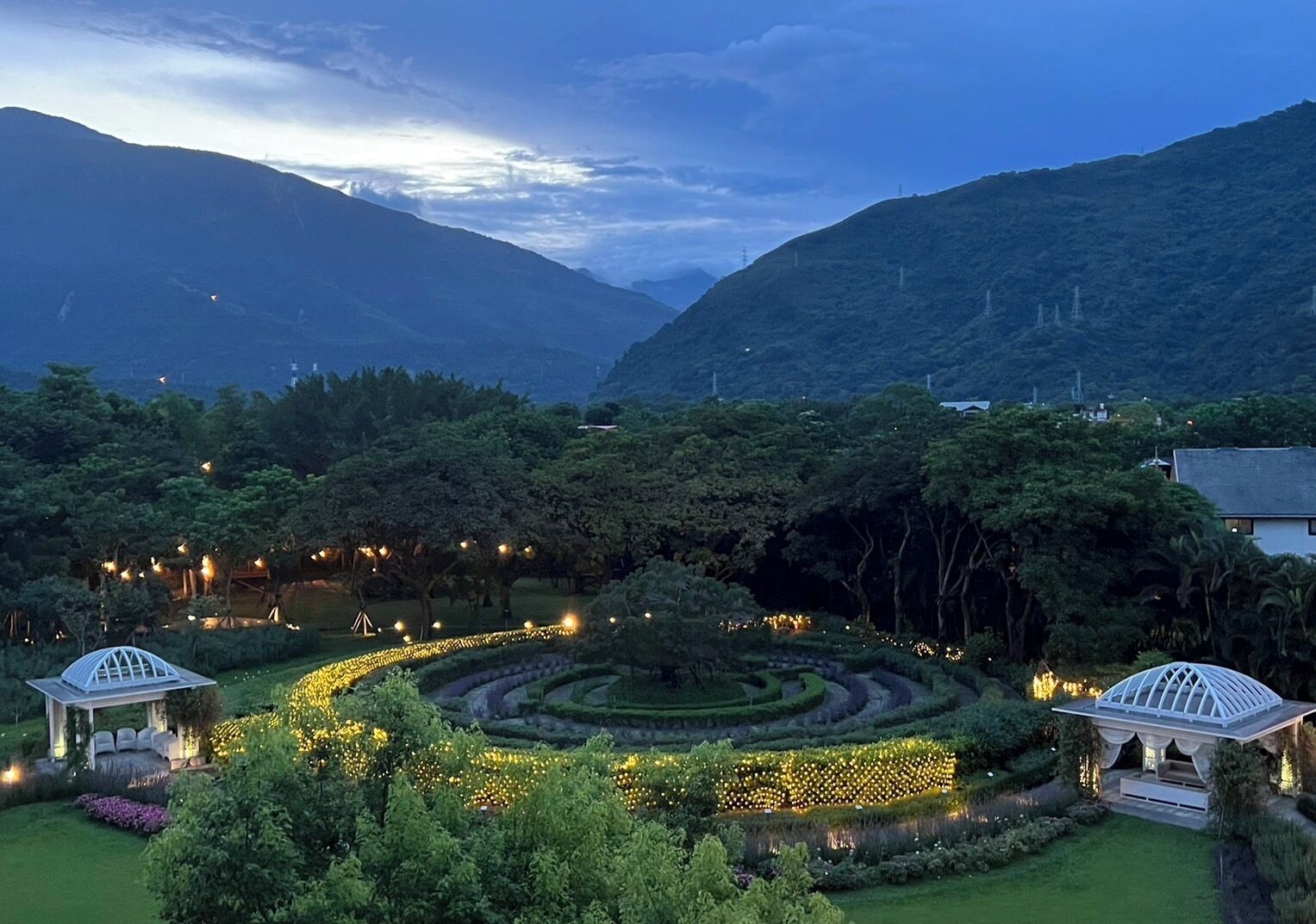 A landscaped garden with a central circular pathway, two gazebos, and surrounding greenery.