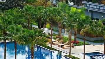A pool area with lounge chairs, palm trees, and a building with a tiled roof.