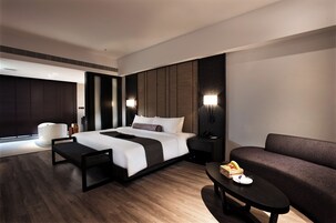 Una habitación de hotel moderna con una cama grande, mesitas de noche, un sofá y una pequeña mesa con una cesta de frutas.