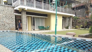 En swimmingpool med ett rutmönstrat kakel, en stenmur och en byggnad med en balkong i bakgrunden.