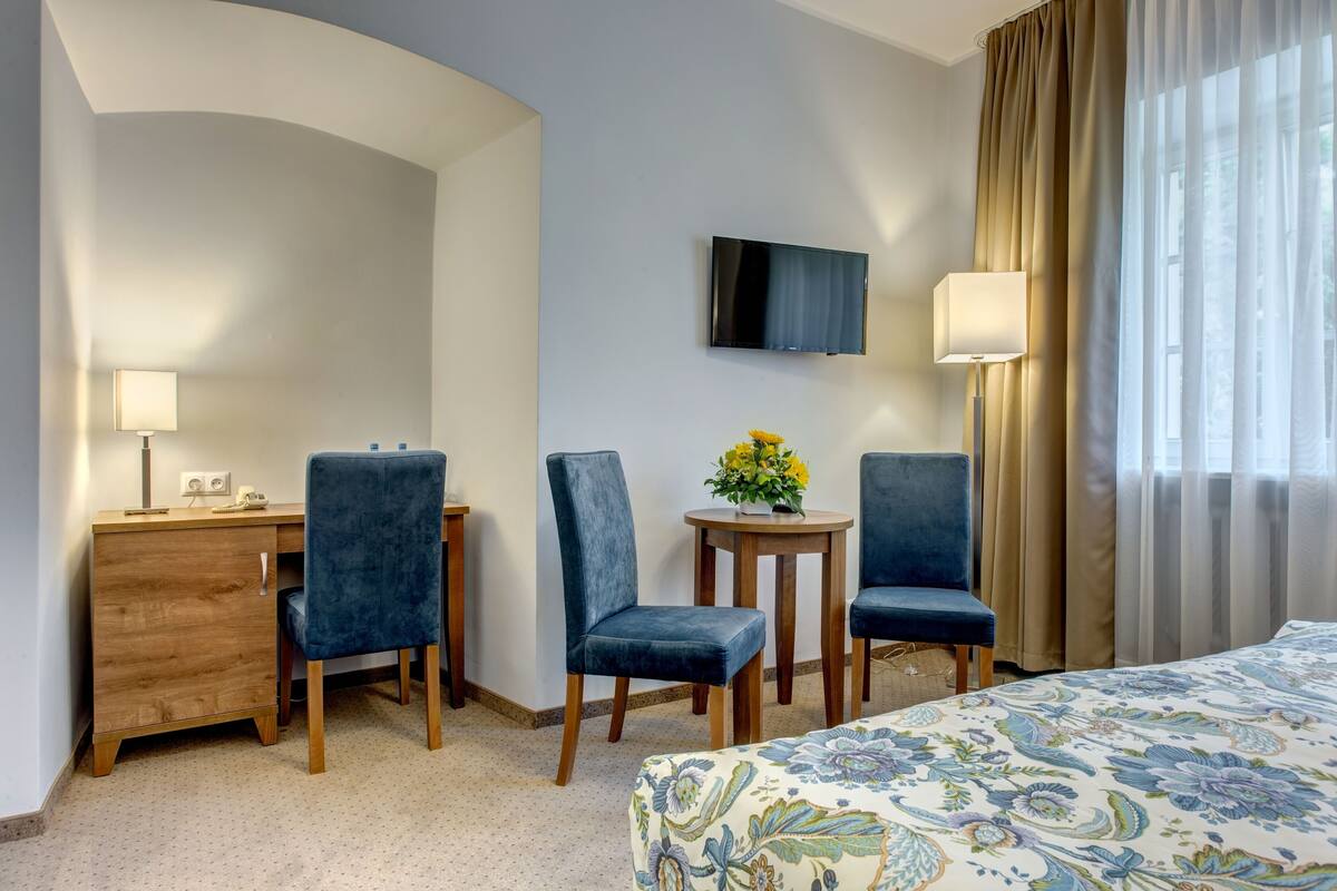 Ein Hotelzimmer mit einem Bett, zwei Stühlen, einem Schreibtisch, einem Fernseher und einem kleinen Tisch mit Blumen.