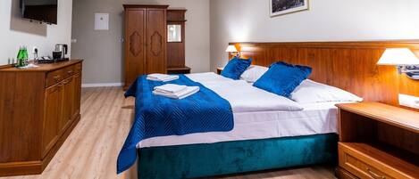 A hotel room with a bed, a wooden wardrobe, a TV mounted on the wall, and a framed picture on the wall.