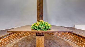 A wooden table with a floral arrangement on top, set against a brick wall with a patterned floor.