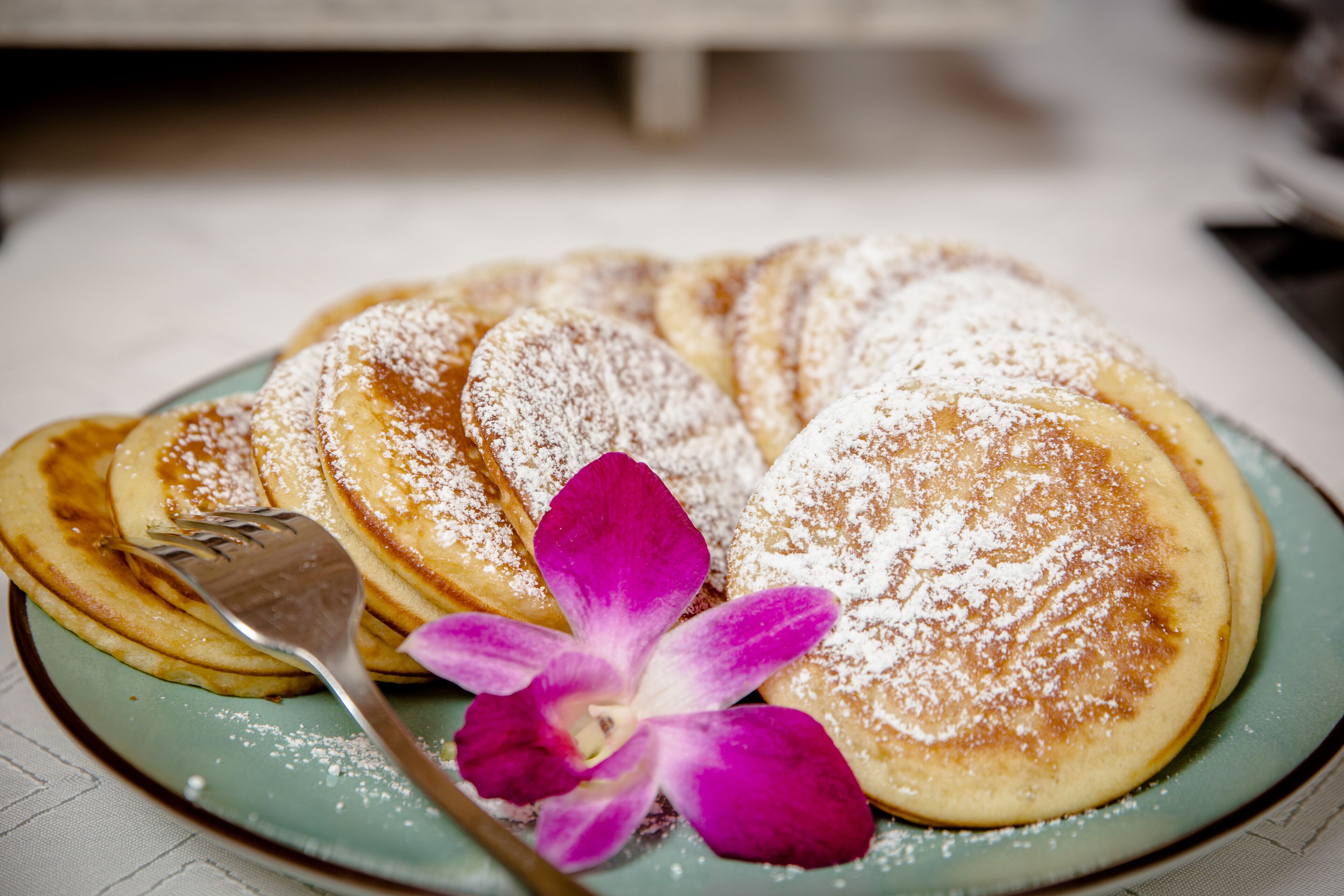 A plate of pancakes with powdered sugar and a purple flower.