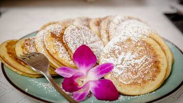 A plate of pancakes with powdered sugar and a purple flower.