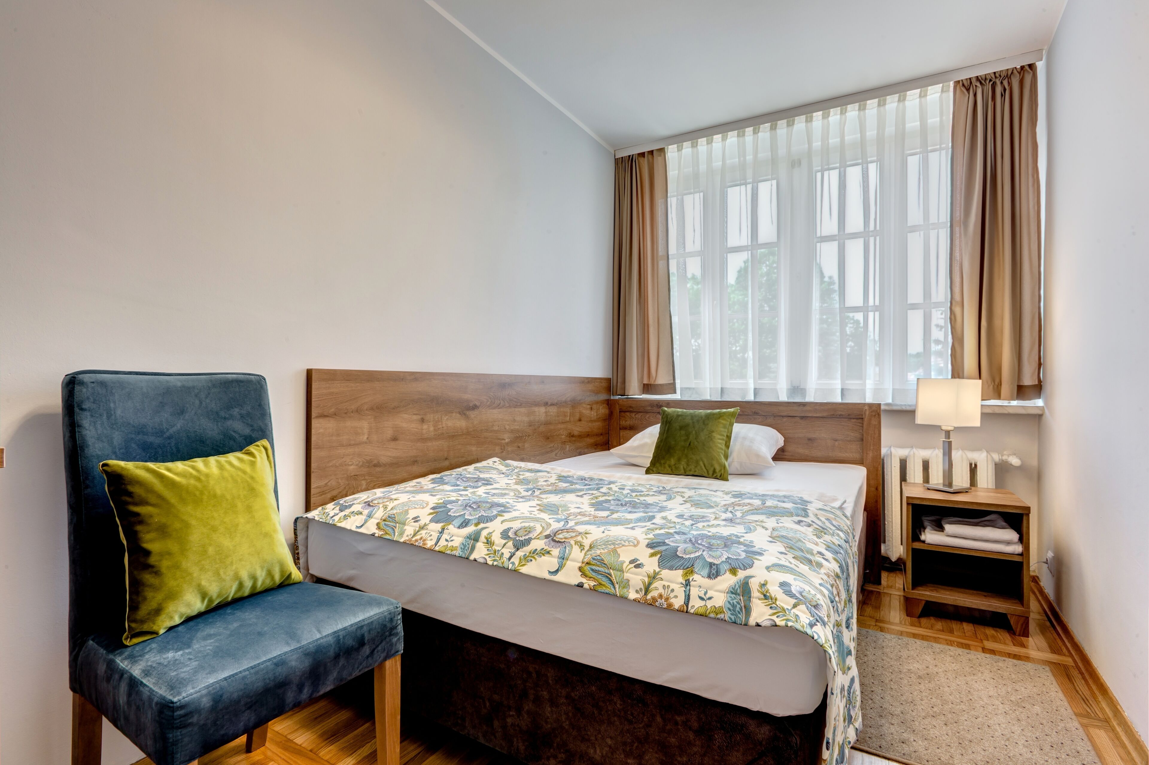 Habitación de hotel con cama, una silla, una mesita de noche y un ventanal con cortinas.