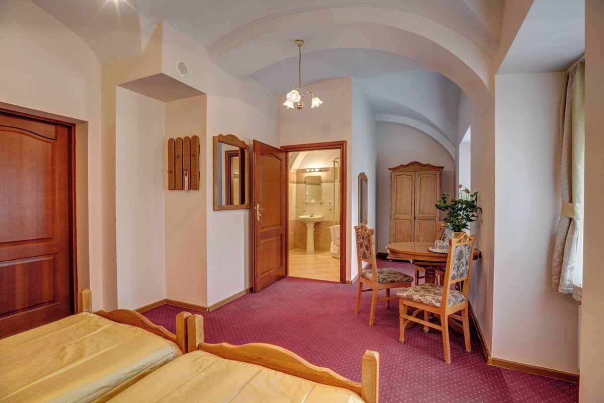 Ein Schlafzimmer mit einem Bett, einem Holzschrank, einem Schreibtisch mit Stuhl und einem durchgehenden Türspalt einsehbaren Badezimmer.