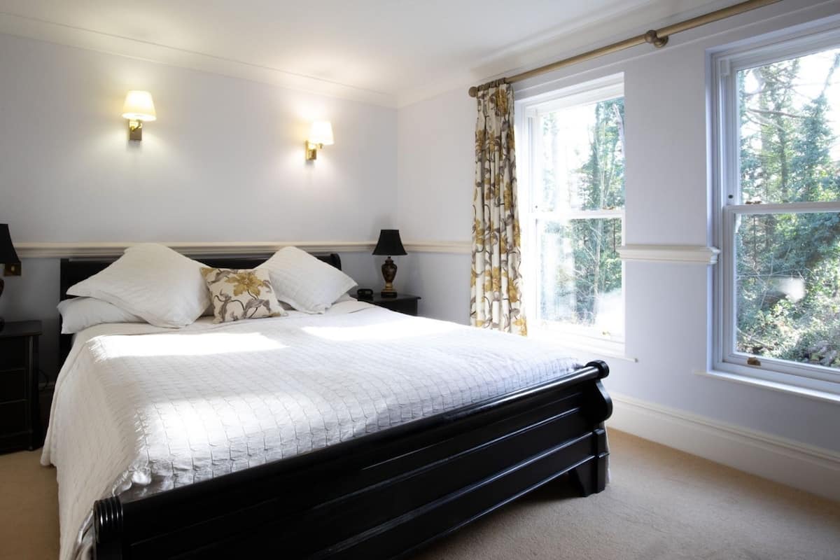 A bedroom with a black bed frame, white bedding, two bedside lamps, a nightstand, and a window with curtains.