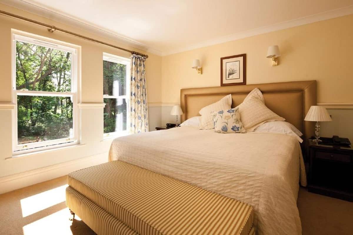A neatly arranged bedroom with a large bed, a bedside table, a lamp, and a window with curtains.