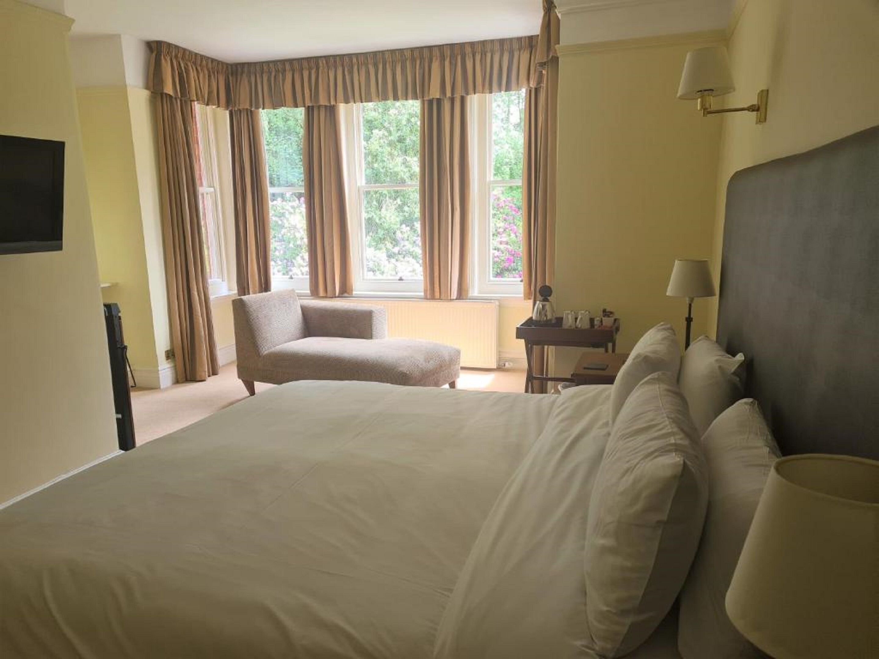 Ein Hotelzimmer mit einem großen Bett, einem Sessel, einem Schreibtisch und einem fenster mit Vorhängen.