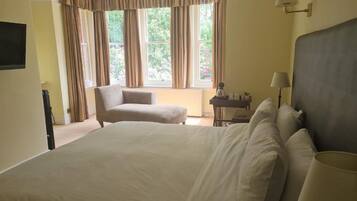 A hotel room with a large bed, a chair, a desk, and a window with curtains.