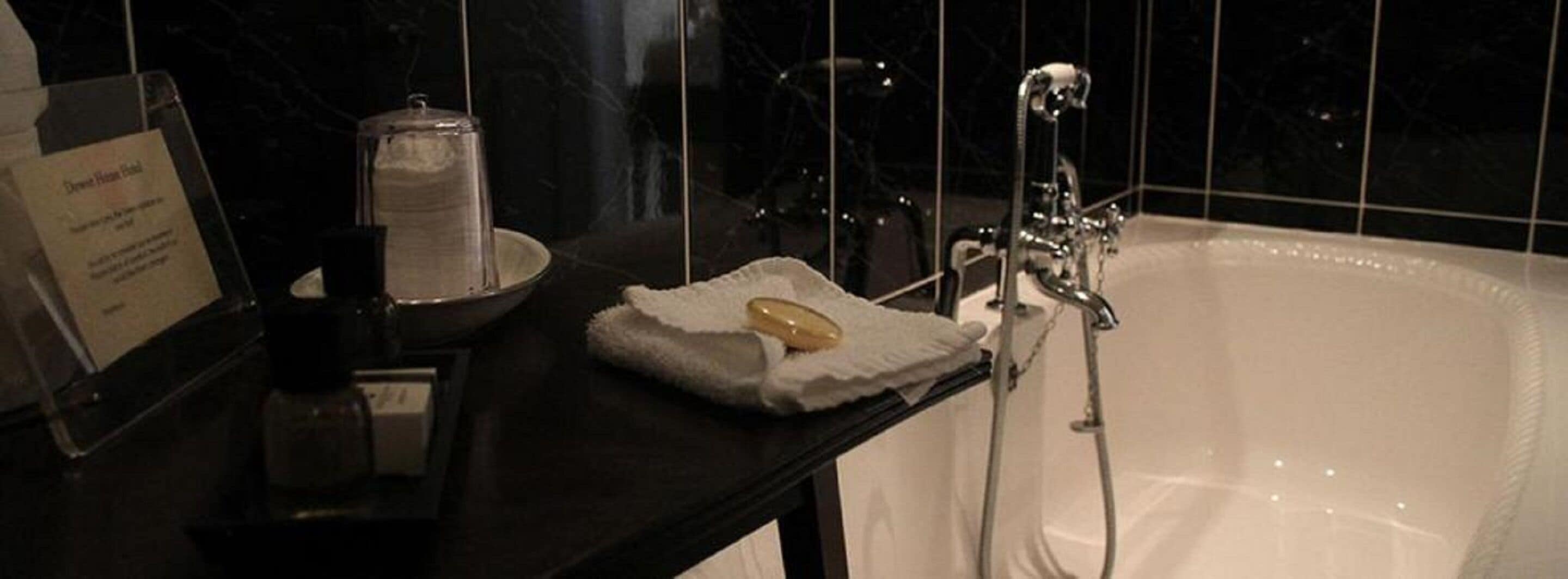 A bathroom with a white bathtub, a towel, and a soap dish on a black countertop.