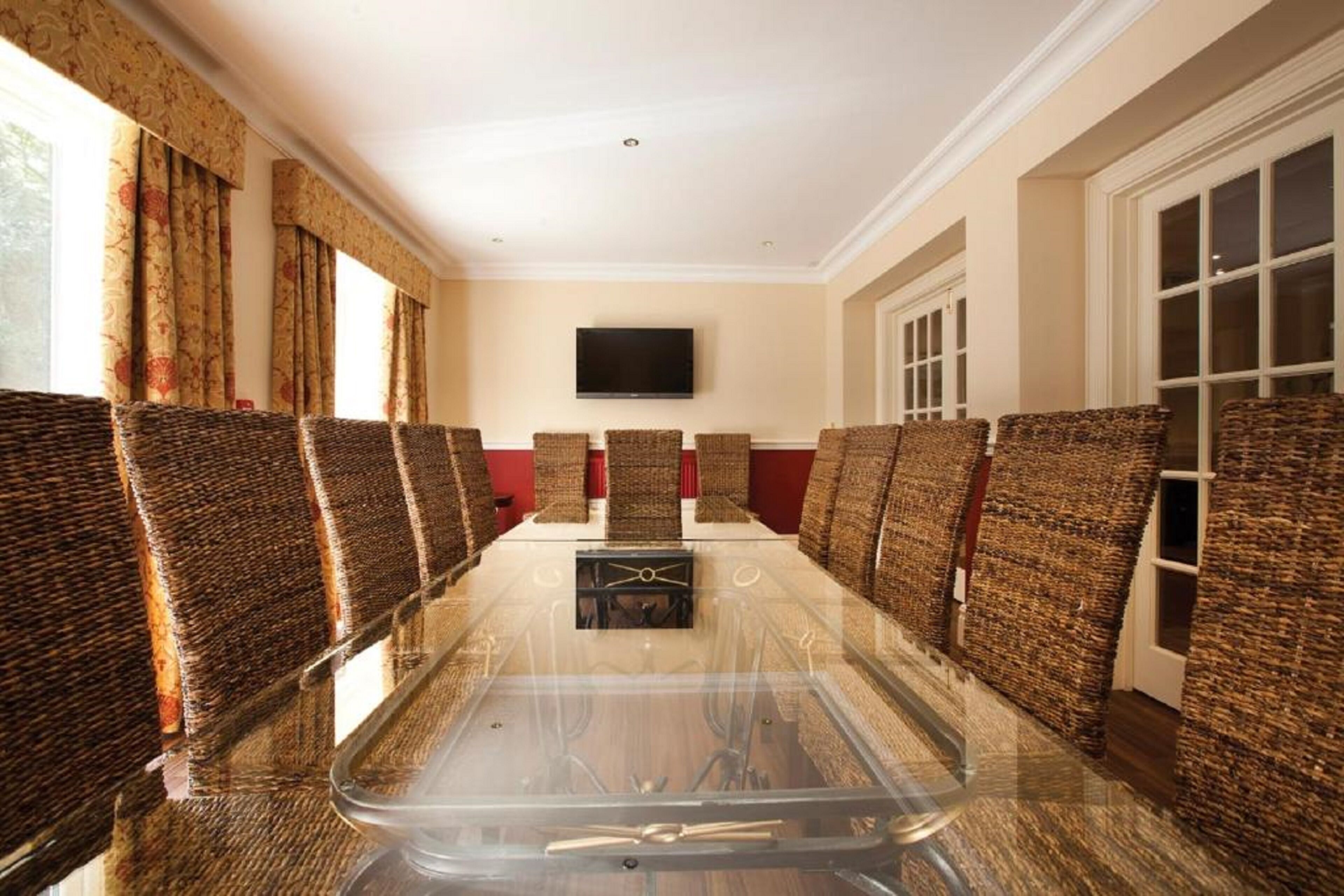 A conference room with a glass table, wicker chairs, a flat-screen TV, and a red accent wall.