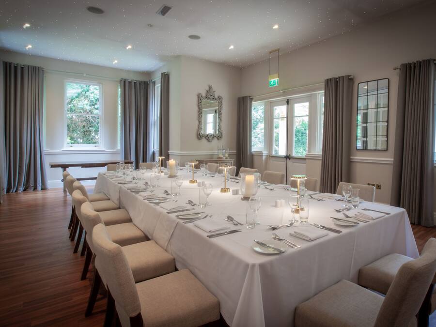 A formal dining room with a long table set for a meal, large windows, and a chandelier.