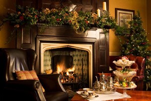 Una habitación acogedora con chimenea, un árbol de Navidad y una mesa servida con té y pasteles.