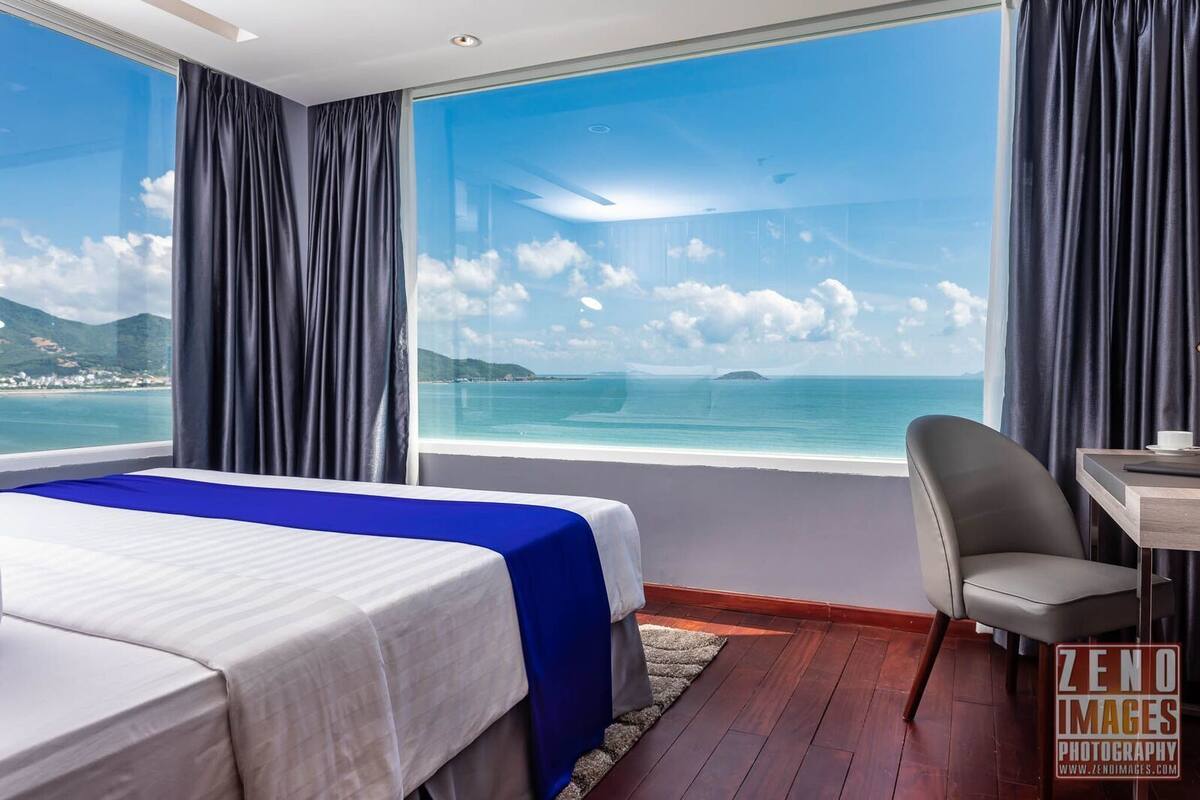 Une chambre d’hôtel dotée d’une grande fenêtre donnant sur la mer et sur le paysage lointain.
