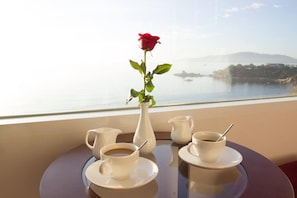 A table with a vase of a red rose and two cups of coffee, set against a scenic view of a body of water and distant land. - Truong Hotel (Bac Nha Trang)