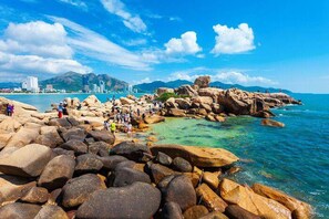 A rocky beach with clear water and people enjoying the view. - Truong Hotel (Bac Nha Trang)