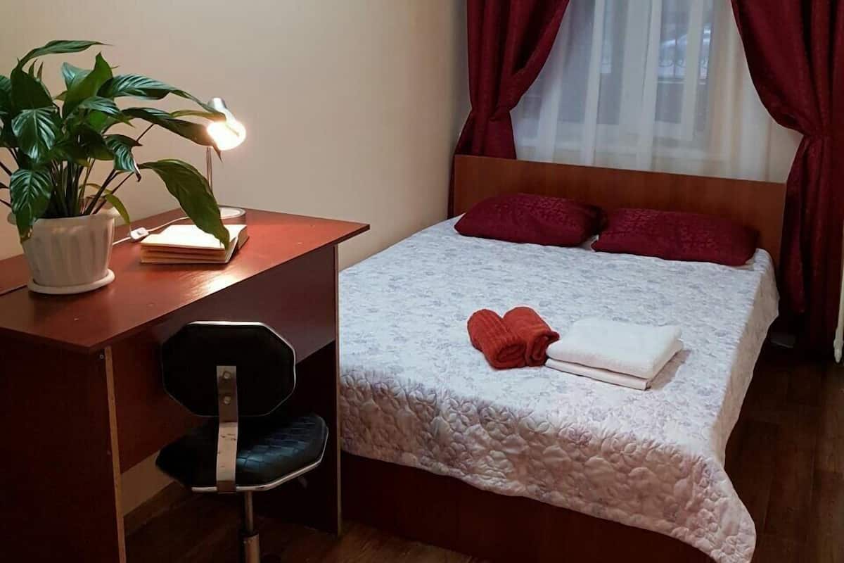 A bedroom with a bed, a desk, a chair, and a potted plant.