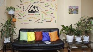 A black leather sofa with colorful cushions, a wall with a map of the world, and several potted plants. - FM Hostel Almaty (Almaty)