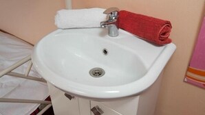 A white pedestal sink with a silver faucet, a white towel, and a red towel on a white towel rack. - FM Hostel Almaty (Almaty)