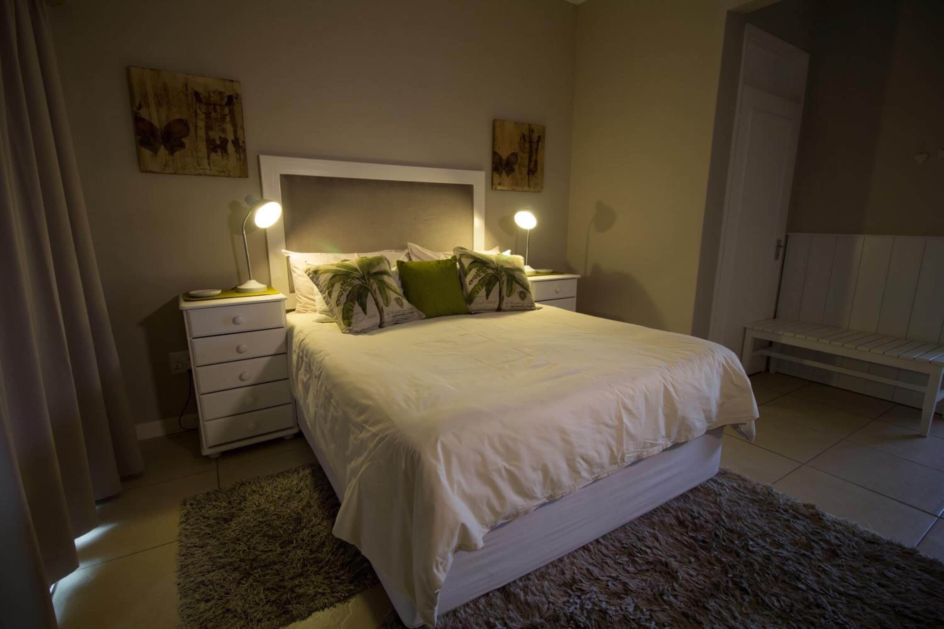 Un dormitorio con cama, mesitas de noche, un banco y obras de arte en las paredes.