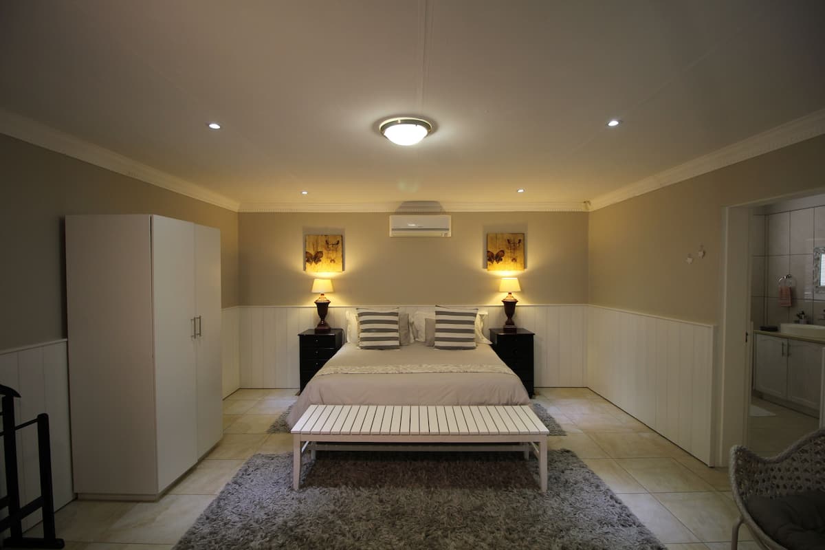 Een slaapkamer met een bed, nachtkastjes, een bankje, een kledingkast en een keukenhoek.