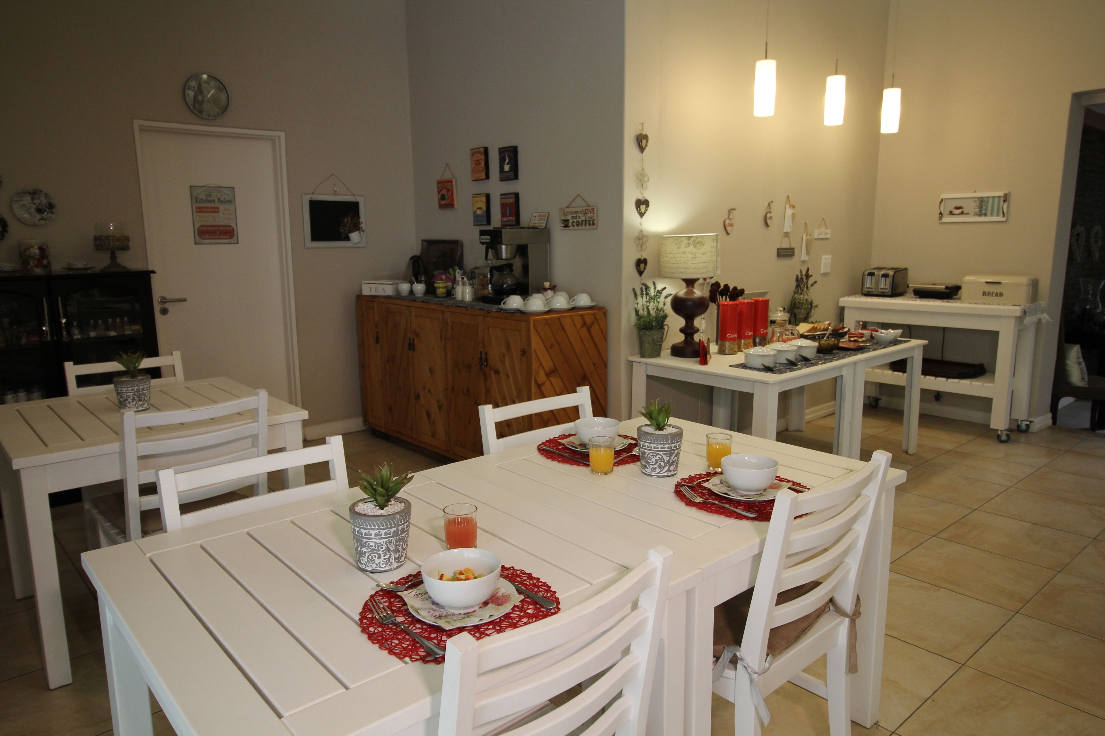 Un comedor con mesas y sillas blancas, una máquina de café y diversos electrodomésticos de cocina.