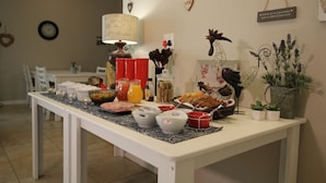 Een ontbijttafel gedekt met diverse soorten eten en drinken, omringd door stoelen en een lamp.