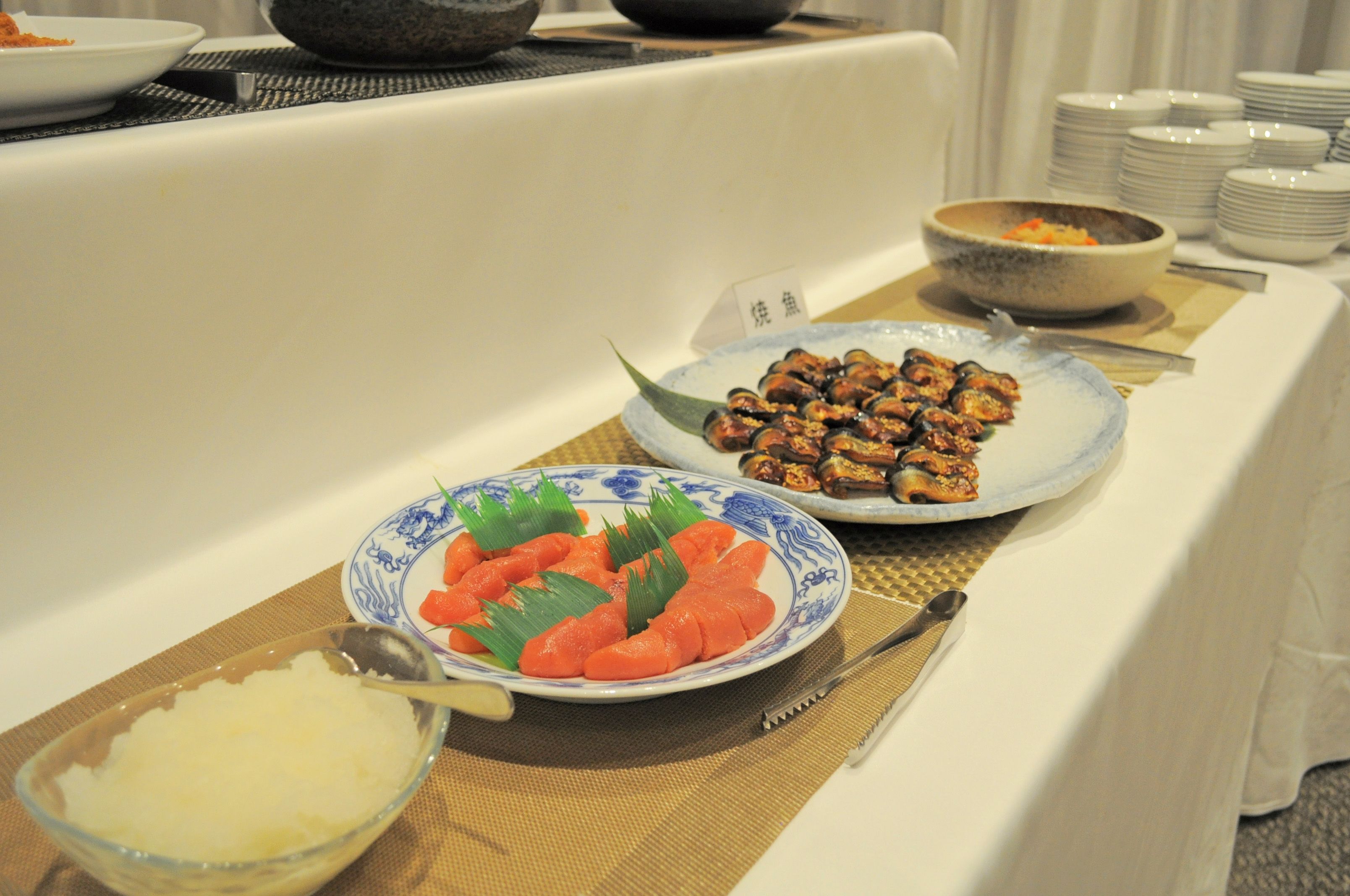 A buffet table with various dishes, including a bowl of rice, a plate of sashimi, and a bowl of soup.
