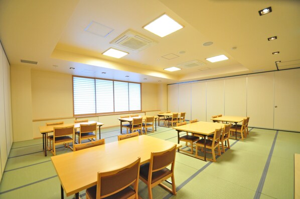 A conference room with multiple tables and chairs, large windows with blinds, and recessed ceiling lights. - Rikuchu Kaigan Grand Hotel (Kamaishi)