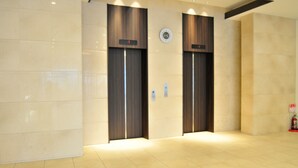 A modern elevator area with two elevators, a wall-mounted clock, and a fire extinguisher. - Rikuchu Kaigan Grand Hotel (Kamaishi)