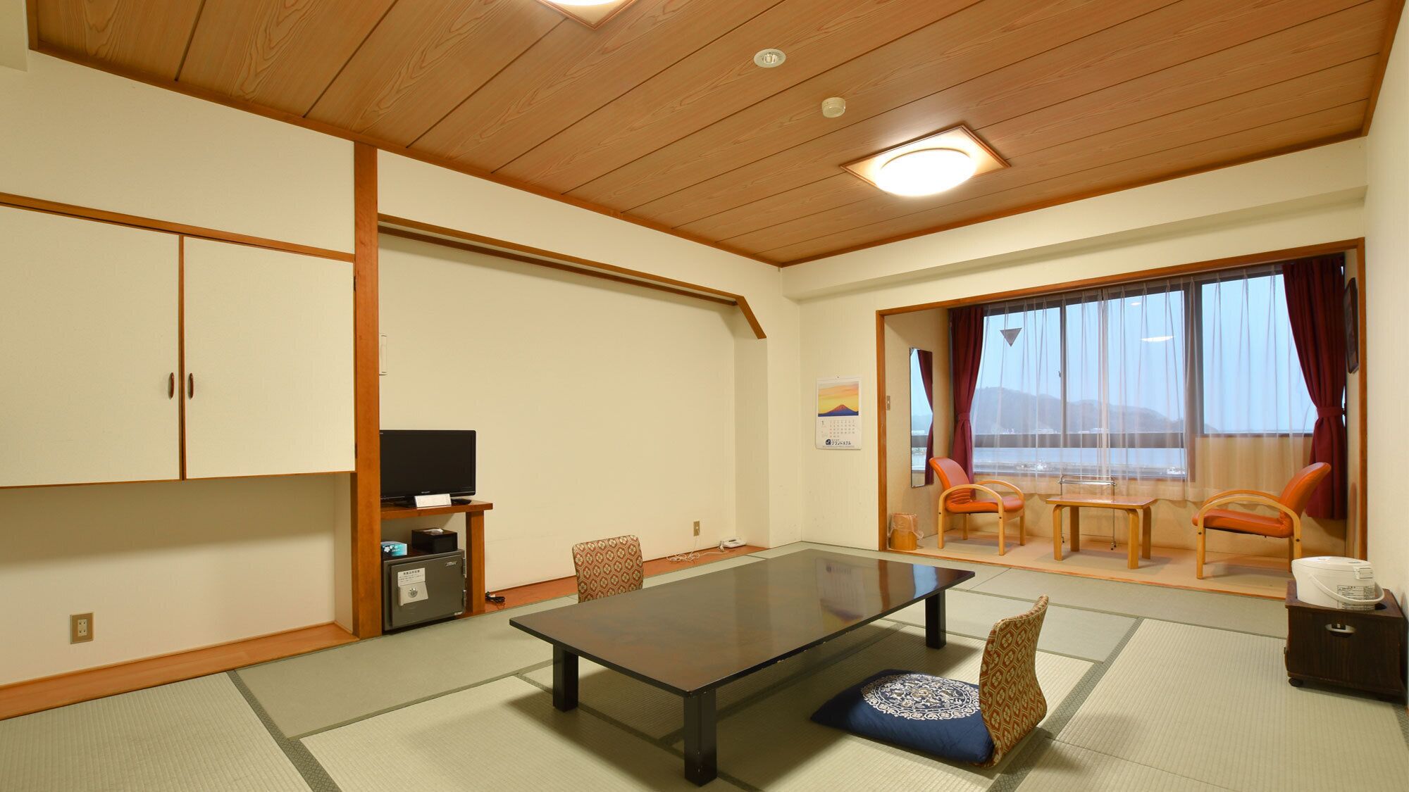 Una tipica stanza giapponese con pavimento in tatami, un tavolino, un televisore e porte scorrevoli che danno su un balcone.