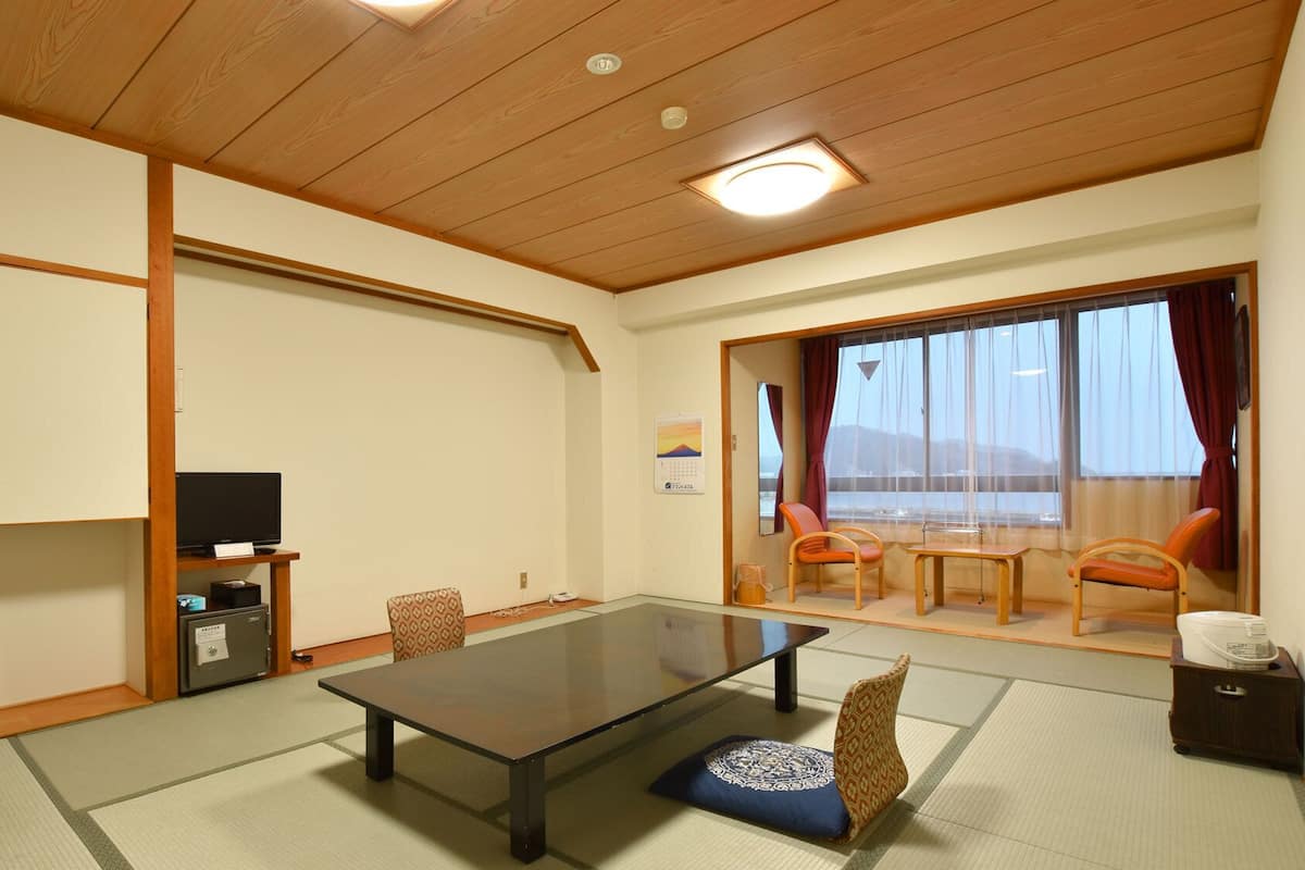 A traditional Japanese room with tatami flooring, a low table, a television, and sliding doors leading to a balcony.