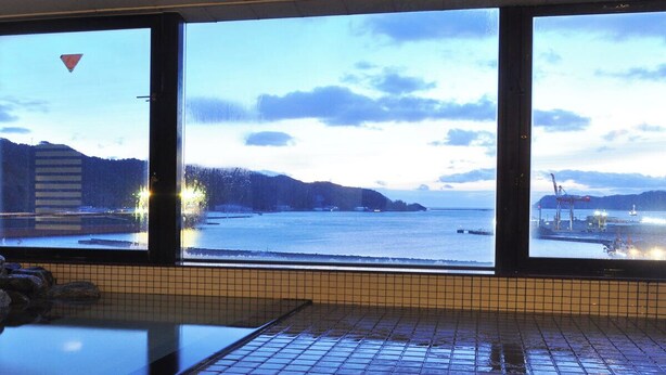 A room with a large window overlooking a body of water, a tiled floor, and a bench. - Rikuchu Kaigan Grand Hotel (Kamaishi)