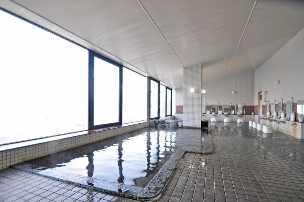 A large indoor swimming pool with clear windows on one side, tiled walls, and a tiled floor.