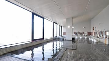 Una gran piscina interior con ventanales amplios, paredes y suelo de cerámica.